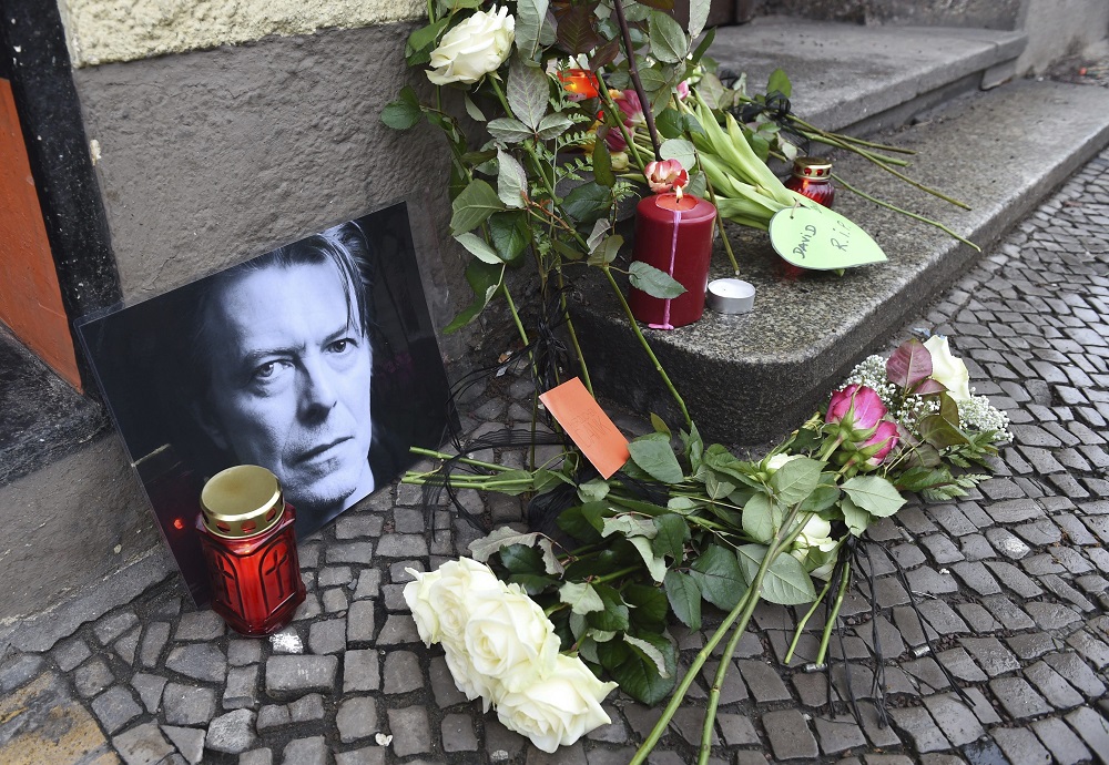 SAB361 BERLÍN (ALEMANIA) 11/01/2016.- Fans depositan flores y velas junto a una foto el cantante británico David Bowie en un altar improvisado frente a su antigua residencia en la Hauptstrasse 155 de Berlín (Alemania), el 11 de enero de 2016. El legendario músico británico David Bowie, autor de clásicos como "Starman" y "Space Oddity", ha muerto a los 69 años de cáncer, informa hoy su página de Facebook. Según este mensaje, el artista, que popularizó el "glam rock" en los años 70 y 80, falleció este domingo "serenamente, rodeado de su familia, tras una valiente batalla de 18 meses contra el cáncer". EFE/Jens Kalaene