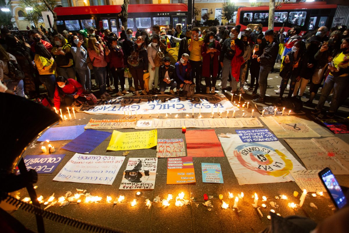 La imagen muestra un grupo de personas reunidos frente a velas y carteles en apoyo a Colombia. 