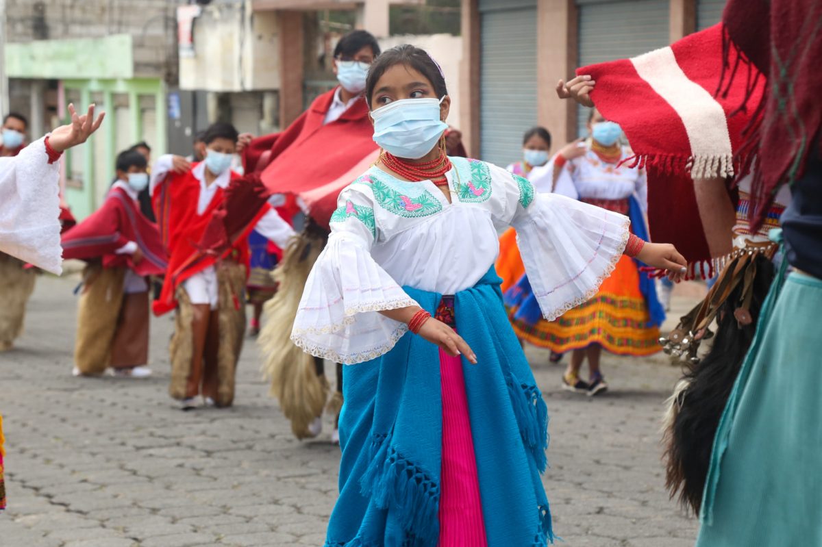La foto muestra a varios jóvenes bailando en las calles de Cayambe, usando mascarillas. 