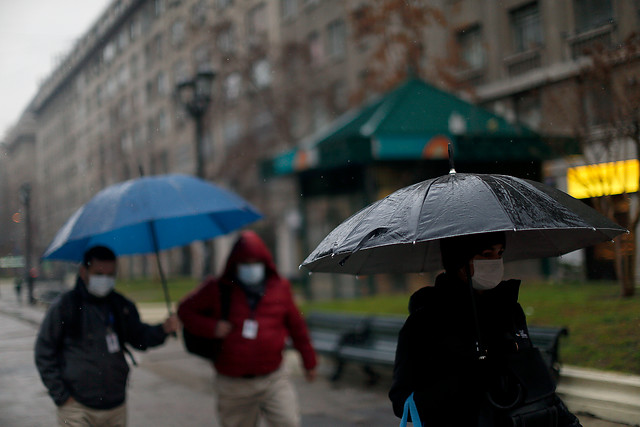 Unas personas caminan con unos paraguas para protegerse bajo la lluvia , durante la cuarentena en el Gran Santiago.