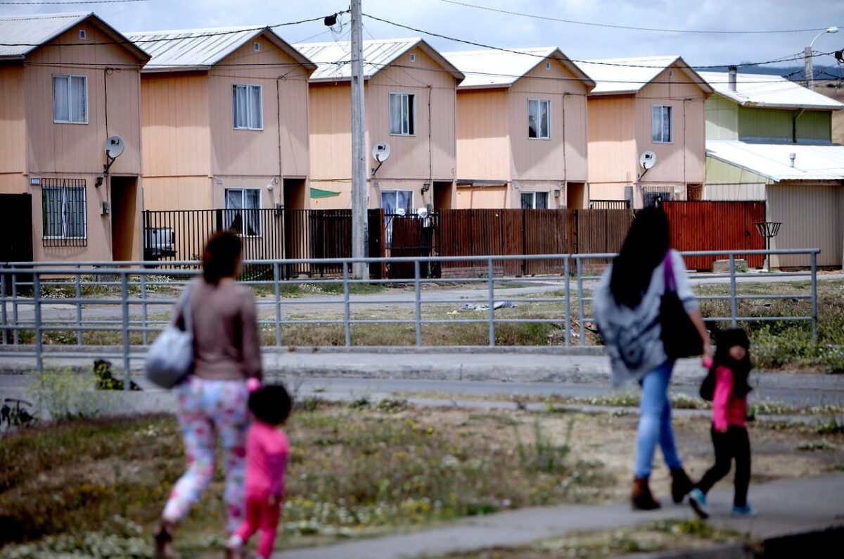 La imagen muestra a un grupo de personas caminando frente a algunas viviendas