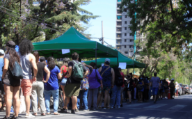 La imagen muestra a decenas de personas bajo el sol haciendo fila para votar