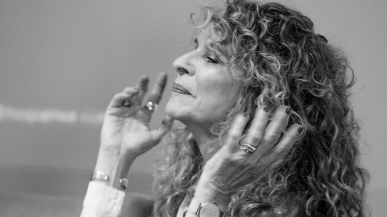 La imagen en blanco y negro muestra a la escritora Gioconda Belli de perfil, con las manos alzadas